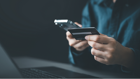 Mãos a segurar um telemóvel e um cartão de crédito, representando fraudes financeiras online.